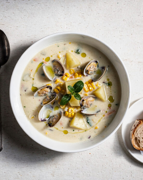 A creamy bowl of corn and clam chowder topped with fresh chives, steam rising in soft natural light.