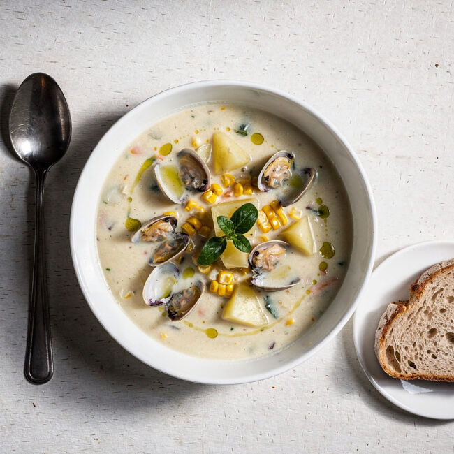 A creamy bowl of corn and clam chowder topped with fresh chives, steam rising in soft natural light.