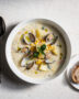 A creamy bowl of corn and clam chowder topped with fresh chives, steam rising in soft natural light.