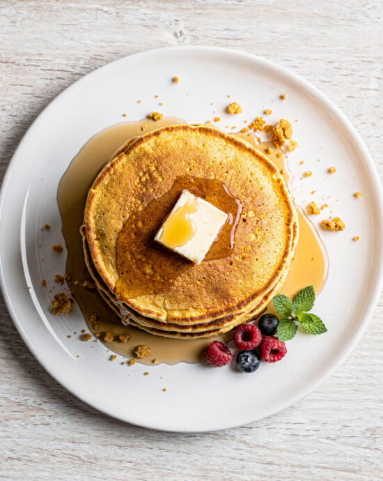 A stack of golden brown cornmeal pancakes drizzled with maple syrup on a rustic wooden board.