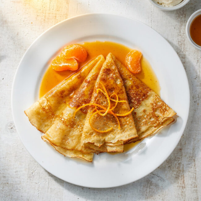 The finished, beautifully sauced crepe suzette recipe served on a classic white plate.