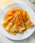 The finished, beautifully sauced crepe suzette recipe served on a classic white plate.