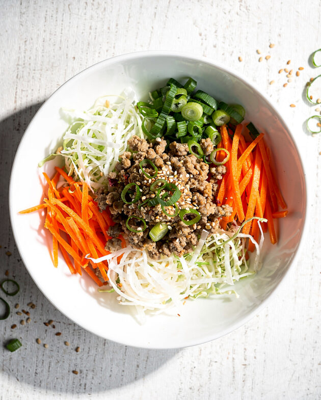 A vibrant, savory skillet of egg roll in a bowl, garnished with green onions and sesame seeds, ready to eat.