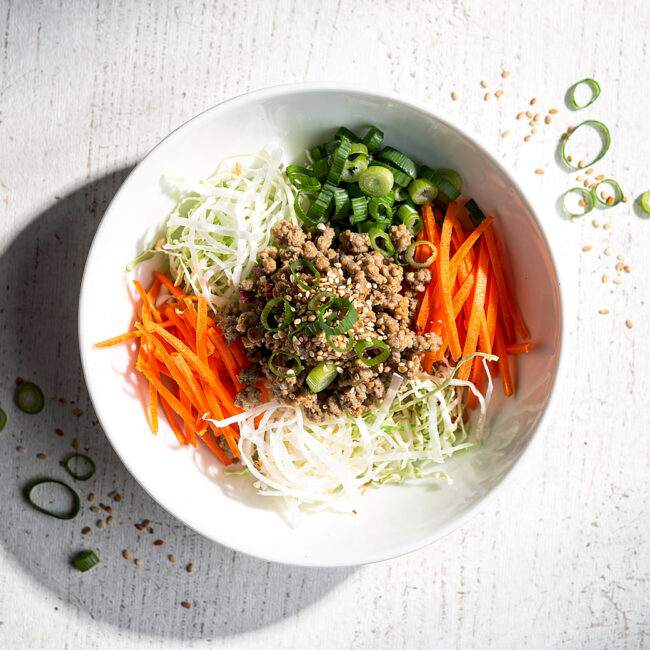 A vibrant, savory skillet of egg roll in a bowl, garnished with green onions and sesame seeds, ready to eat.