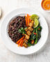 A steaming bowl of feijoada vegetarian with black beans, mushrooms, and plantains, served over rice with orange wedges.