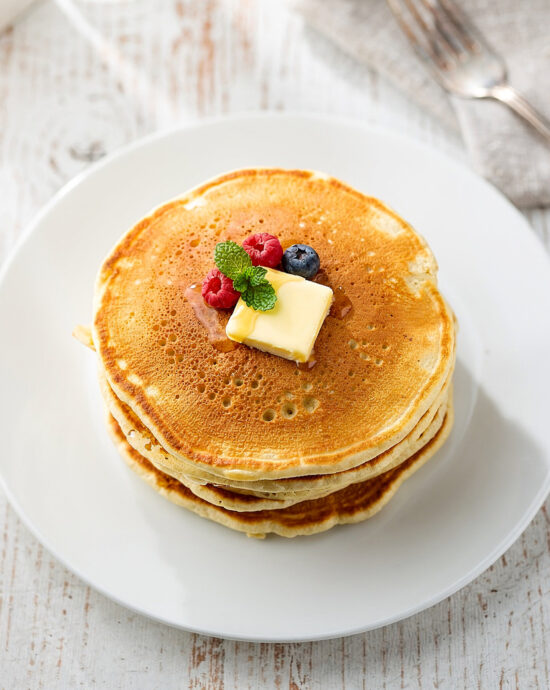 A tall stack of golden brown pancakes from the perfect fluffy pancake recipe, drizzled with maple syrup.