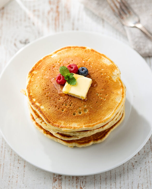 A tall stack of golden brown pancakes from the perfect fluffy pancake recipe, drizzled with maple syrup.