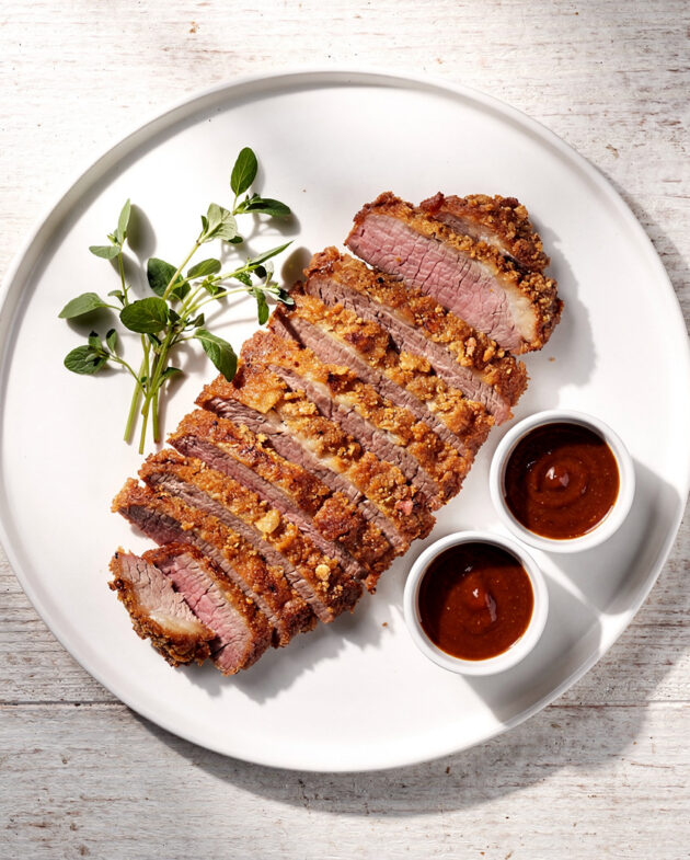 A close-up shot of golden fried brisket fritters with a crispy crust, plated on a rustic wooden board.