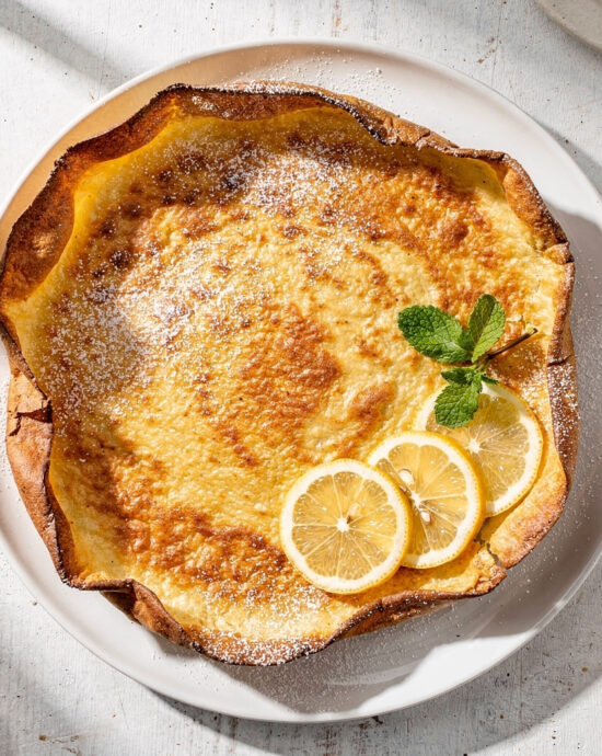 A golden, puffed german pancake recipe fresh from the oven, dusted with powdered sugar.
