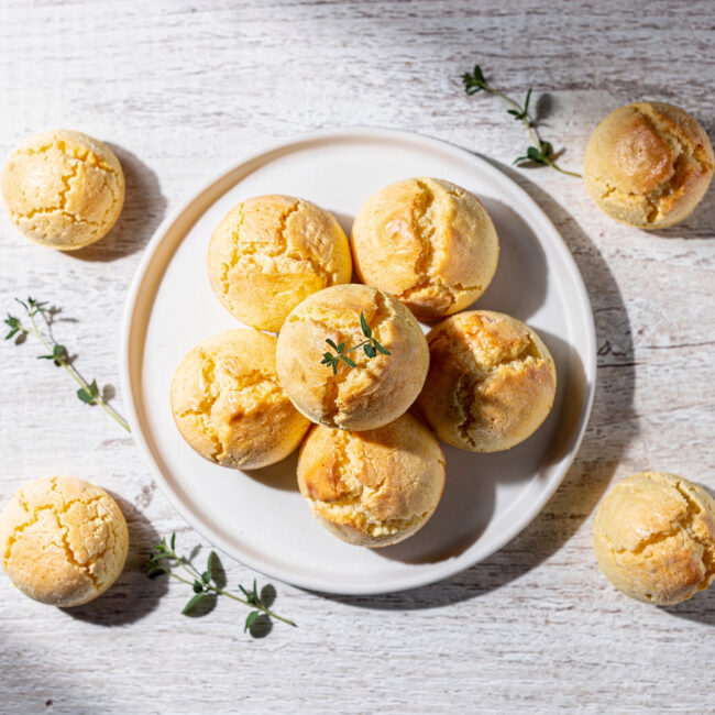 A golden batch of freshly baked gluten free Brazilian cheese bread, perfectly puffed and slightly cracked, sits on a rustic wooden board.