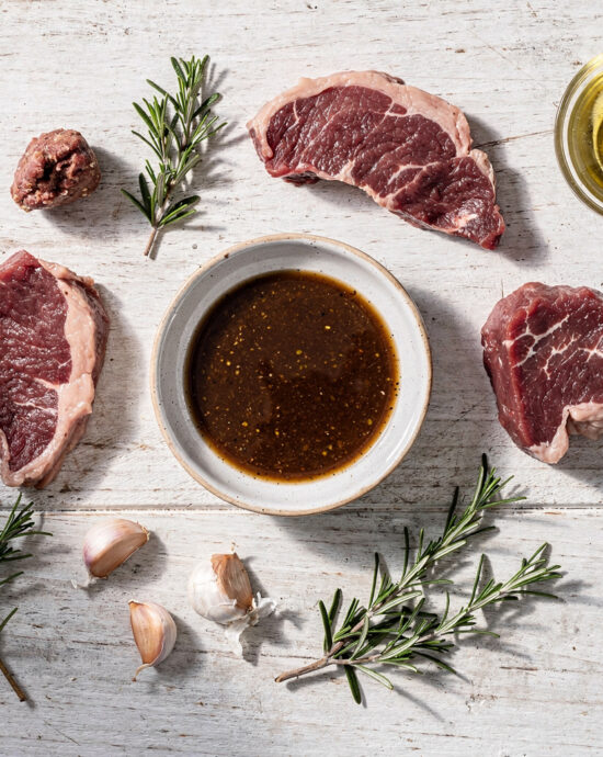 A close-up shot of raw steak soaking in a glossy, herb-flecked gluten-free steak marinade, ready for the grill.