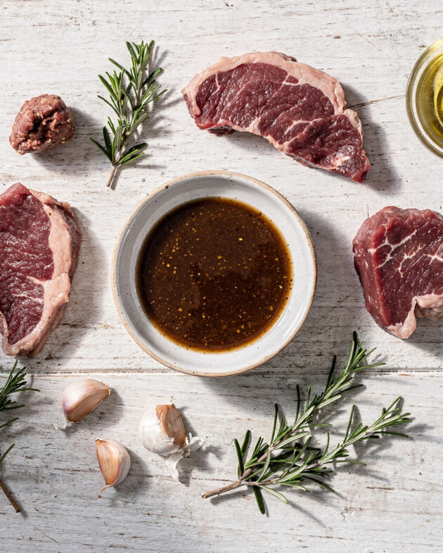 A close-up shot of raw steak soaking in a glossy, herb-flecked gluten-free steak marinade, ready for the grill.