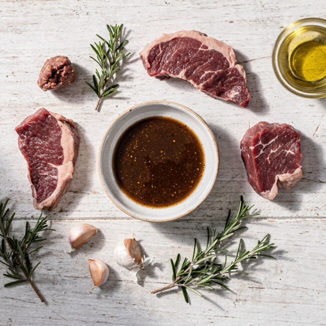 A close-up shot of raw steak soaking in a glossy, herb-flecked gluten-free steak marinade, ready for the grill.