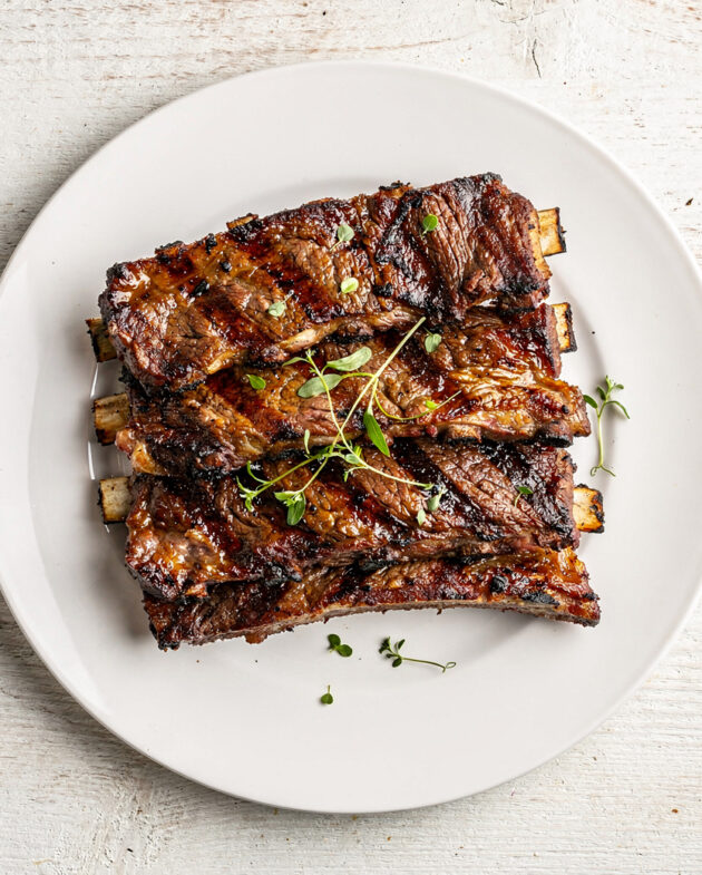 A heaping platter of perfectly grilled beef country style ribs with a glossy, caramelized crust, ready to serve.