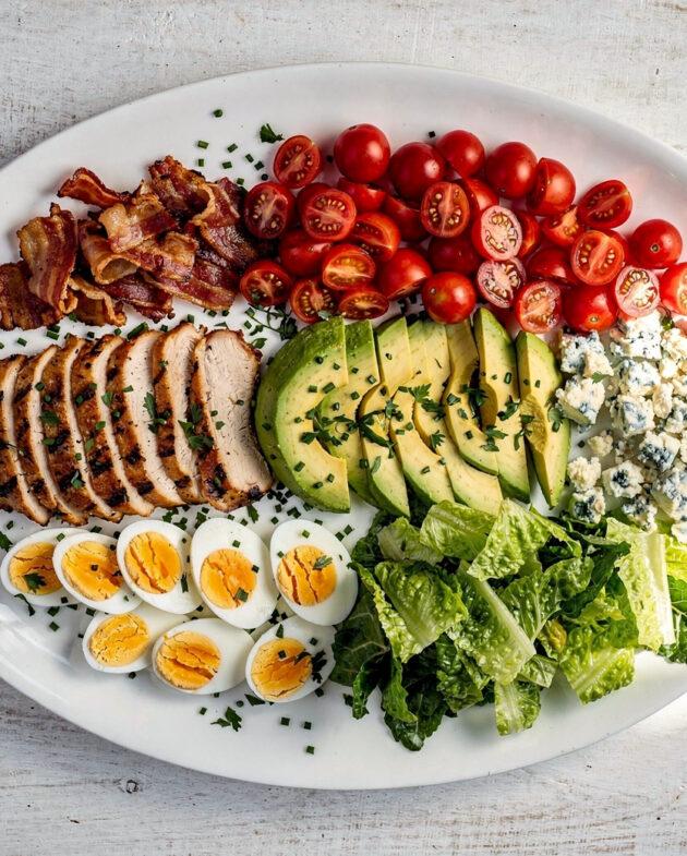 A beautifully plated grilled chicken cobb salad with neat rows of colorful ingredients on a light wood background.