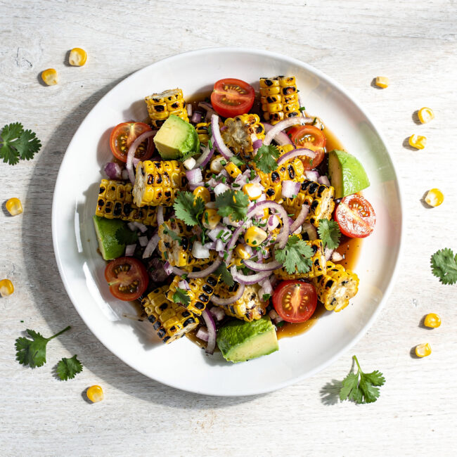 A colorful grilled corn salad with avocado and red onion in a rustic bowl.