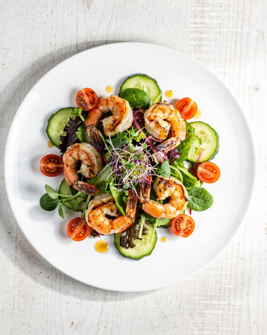 A vibrant grilled shrimp salad featuring charred shrimp, fresh avocado, and sweet corn on a bed of lettuce.
