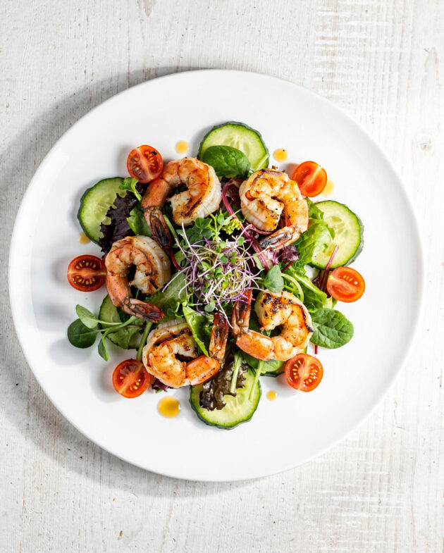 A vibrant grilled shrimp salad featuring charred shrimp, fresh avocado, and sweet corn on a bed of lettuce.