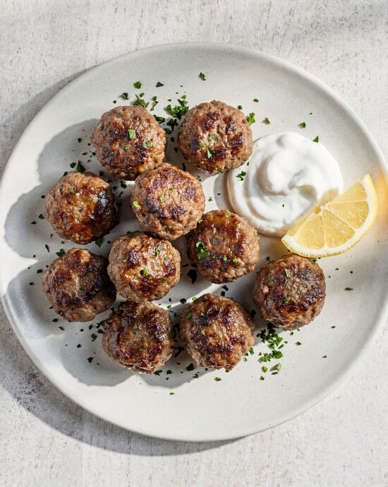 An overhead shot of tender, golden-brown meatballs made from classic ground beef recipes, served with a bright yogurt sauce.