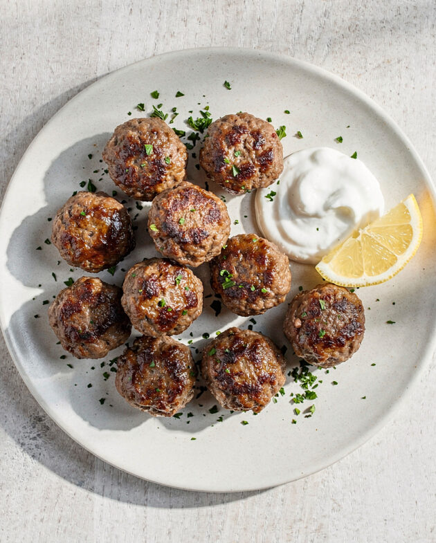 An overhead shot of tender, golden-brown meatballs made from classic ground beef recipes, served with a bright yogurt sauce.