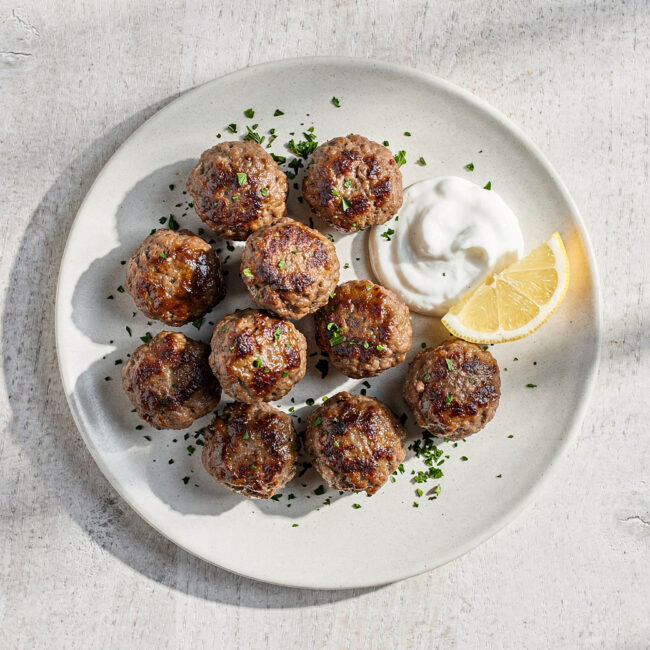 An overhead shot of tender, golden-brown meatballs made from classic ground beef recipes, served with a bright yogurt sauce.