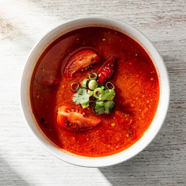 A rich and vibrant tomato soup made with haidilao tomato soup base, garnished with fresh basil and a drizzle of cream in a rustic bowl.