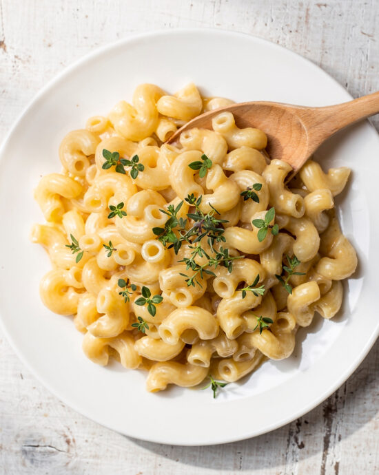 A creamy bowl of healthy mac and cheese topped with fresh herbs and black pepper.