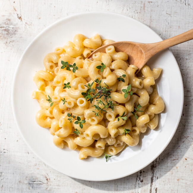 A creamy bowl of healthy mac and cheese topped with fresh herbs and black pepper.