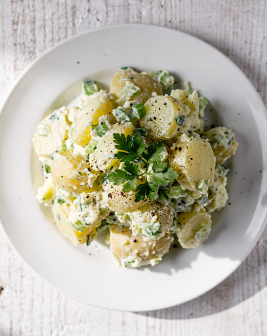 A creamy bowl of homemade potato salad with fresh herbs on a rustic wood table.