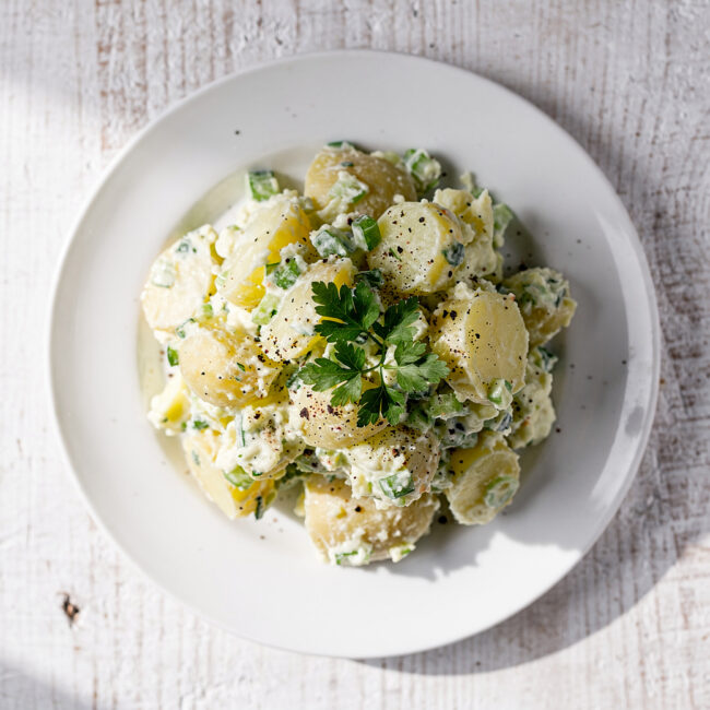 A creamy bowl of homemade potato salad with fresh herbs on a rustic wood table.
