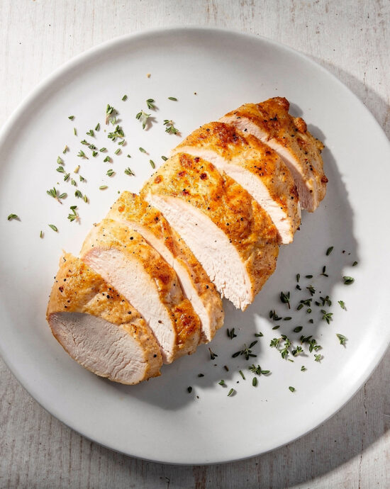 Golden brown, perfectly cooked chicken breast resting on a wooden cutting board, illustrating the answer to how long to cook chicken breast in oven.