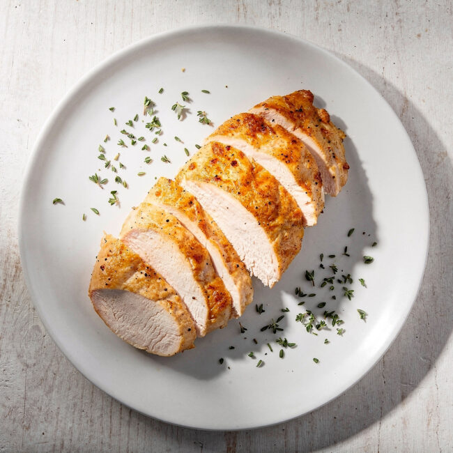 Golden brown, perfectly cooked chicken breast resting on a wooden cutting board, illustrating the answer to how long to cook chicken breast in oven.
