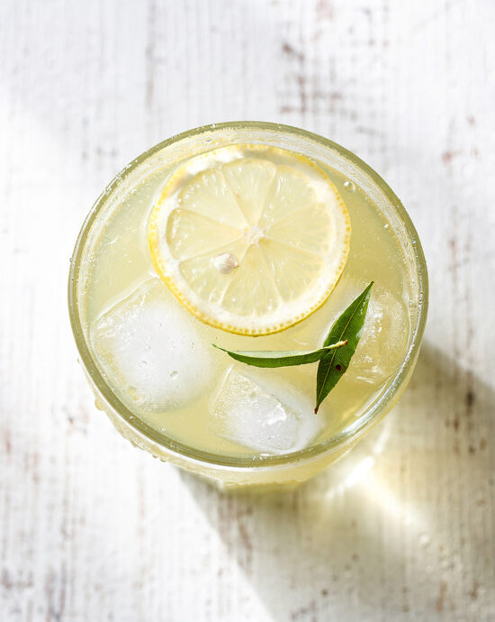 A tall, refreshing glass of iced green tea lemonade garnished with a lemon wheel and mint sprig on a rustic wood table.