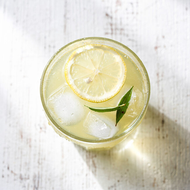 A tall, refreshing glass of iced green tea lemonade garnished with a lemon wheel and mint sprig on a rustic wood table.