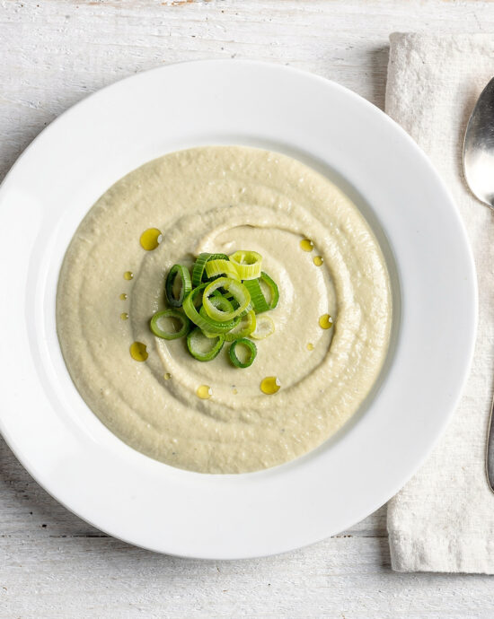 A creamy bowl of leek soup garnished with crispy pancetta and fresh thyme, ready to be enjoyed.