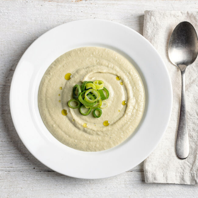 A creamy bowl of leek soup garnished with crispy pancetta and fresh thyme, ready to be enjoyed.