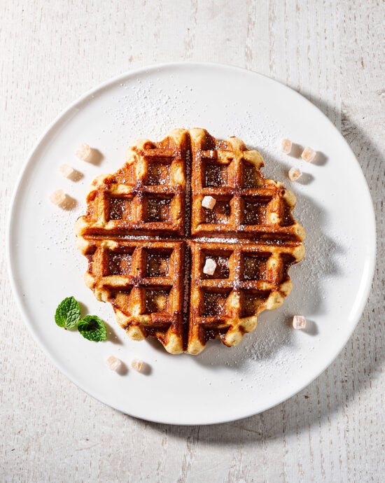 Freshly made liege waffle recipe dusted with powdered sugar on a rustic wooden board.