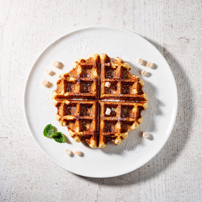 Freshly made liege waffle recipe dusted with powdered sugar on a rustic wooden board.