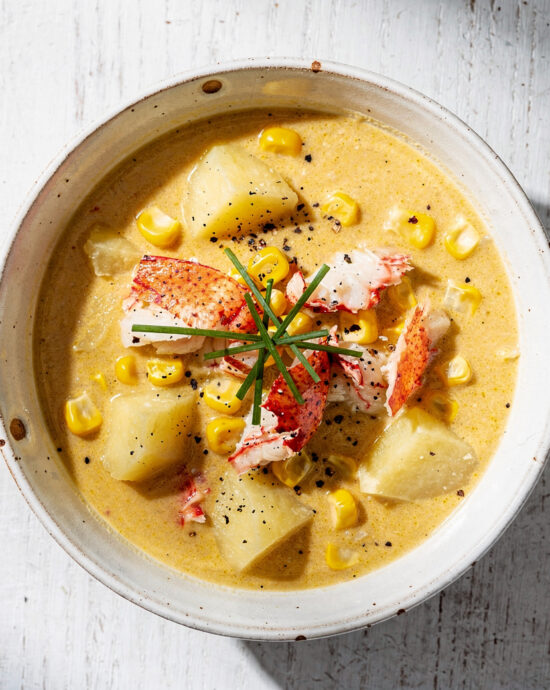 A steaming bowl of rich lobster corn chowder garnished with fresh chives.