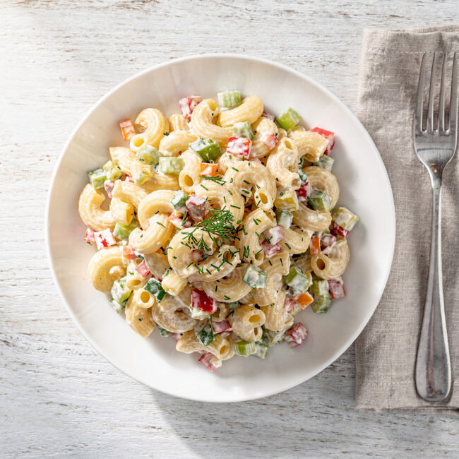 A vibrant, creamy macaroni salad with colorful vegetables, beautifully styled on a rustic wooden table.