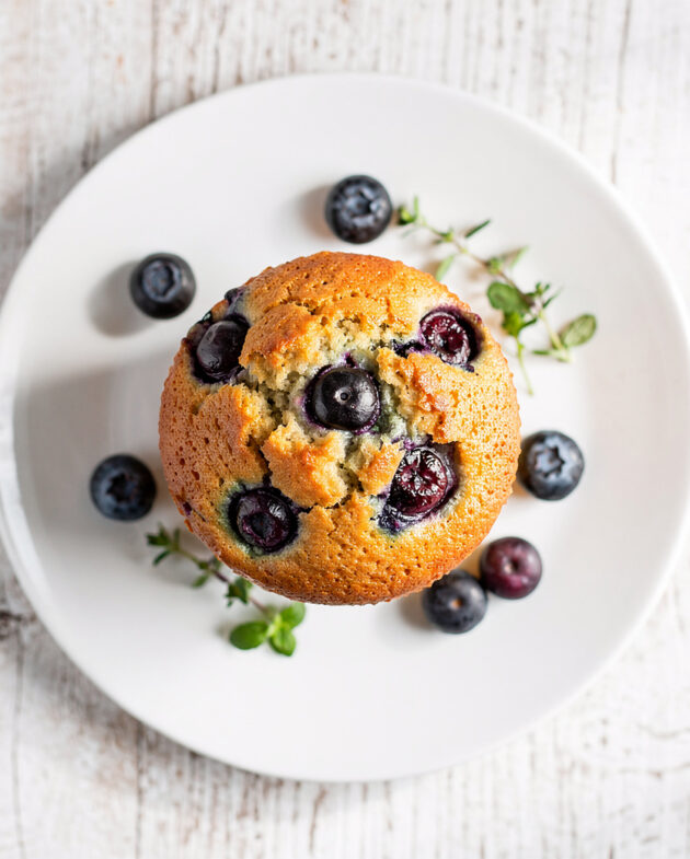 A top-down view of the finished moist blueberry muffin recipe, showing a golden sugar crust and bursting blueberries.