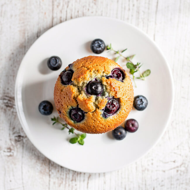 A top-down view of the finished moist blueberry muffin recipe, showing a golden sugar crust and bursting blueberries.
