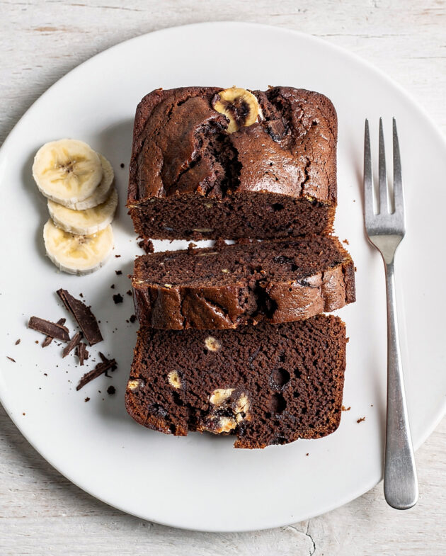 A perfectly baked slice of moist chocolate banana loaf recipe sits on a rustic wood board.