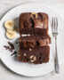 A perfectly baked slice of moist chocolate banana loaf recipe sits on a rustic wood board.