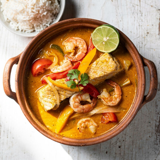 An overhead shot of a vibrant moqueca recipe featuring tender fish and shrimp in a creamy coconut broth, garnished with cilantro and lime.