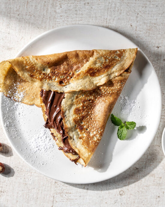 A beautifully plated nutella crepe recipe, dusted with powdered sugar and scattered with fresh raspberries.