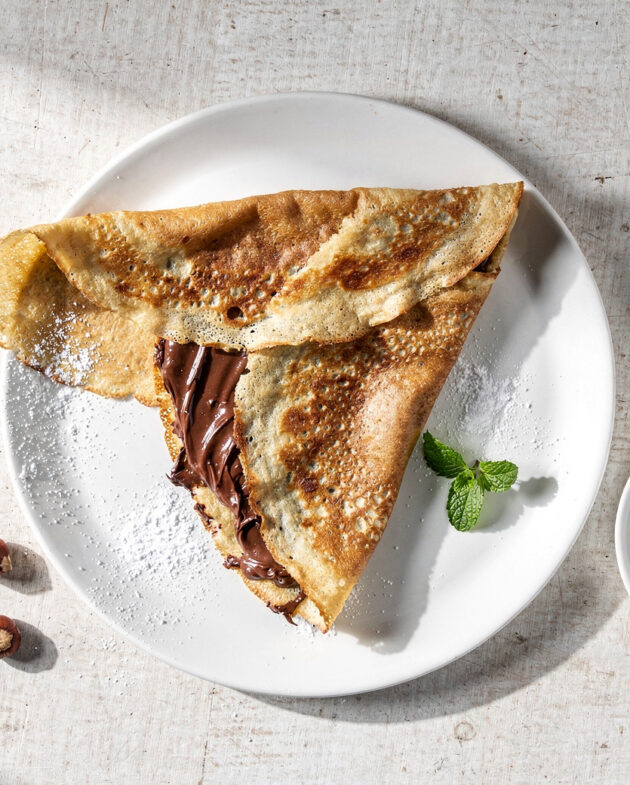 A beautifully plated nutella crepe recipe, dusted with powdered sugar and scattered with fresh raspberries.