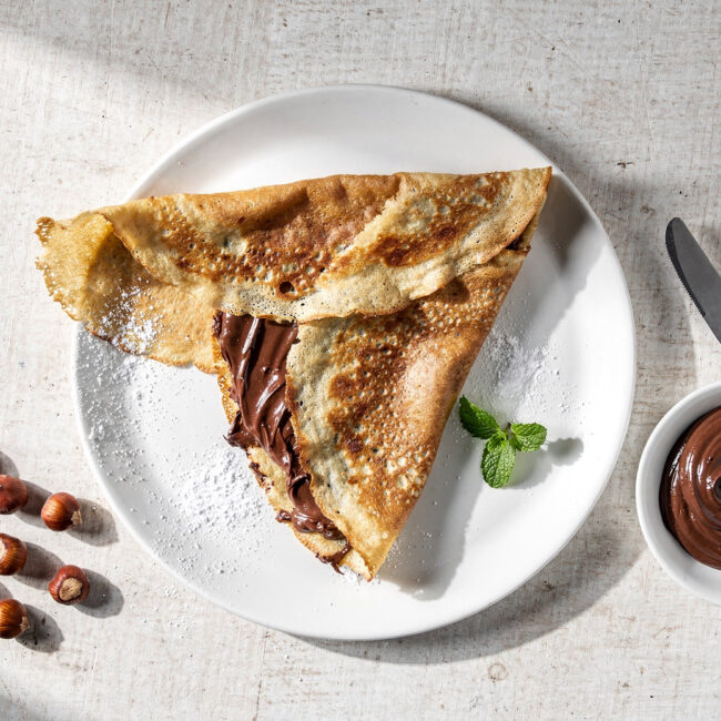 A beautifully plated nutella crepe recipe, dusted with powdered sugar and scattered with fresh raspberries.