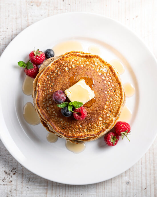 A delicious stack of golden-brown oatmeal pancakes, drizzled with maple syrup and topped with fresh berries.