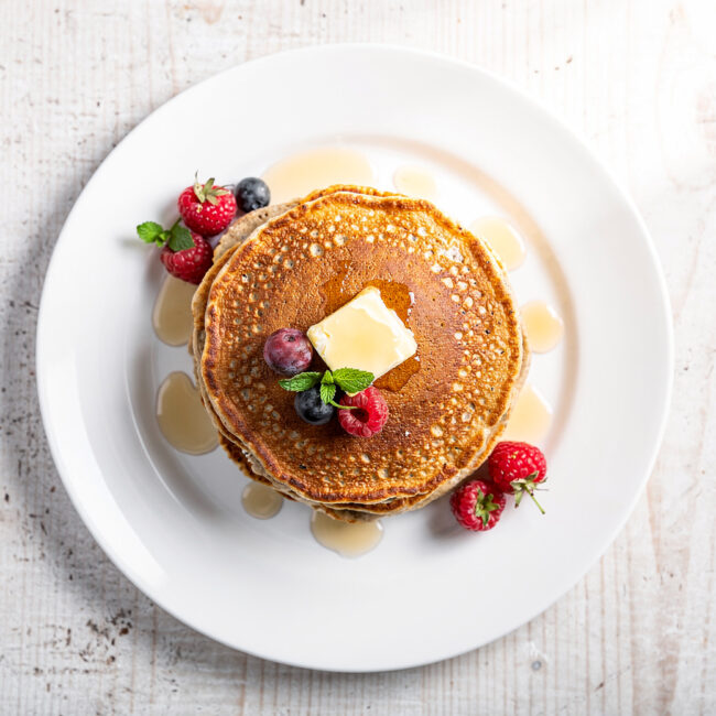 A delicious stack of golden-brown oatmeal pancakes, drizzled with maple syrup and topped with fresh berries.